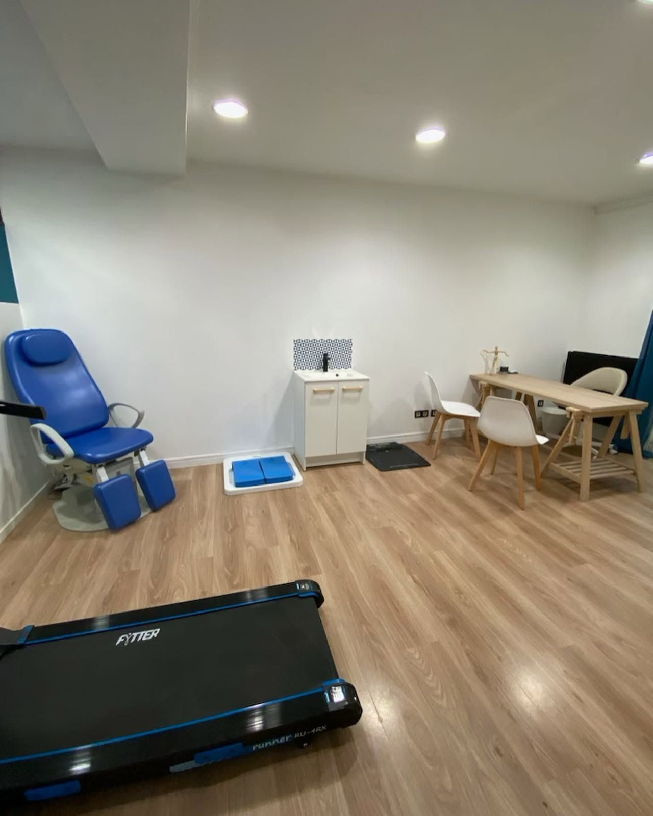 Salon avec fauteuil de consultation bleu, table basse, ensemble de salle à manger et aspirateur robot sur parquet