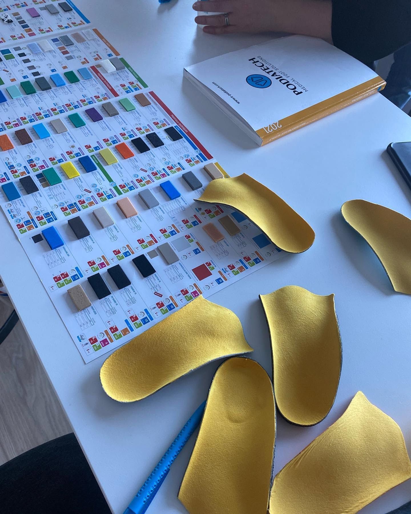 Des échantillons de semelles dorés disposés sur une table à côté d'un nuancier et d'un catalogue Podiatech.
