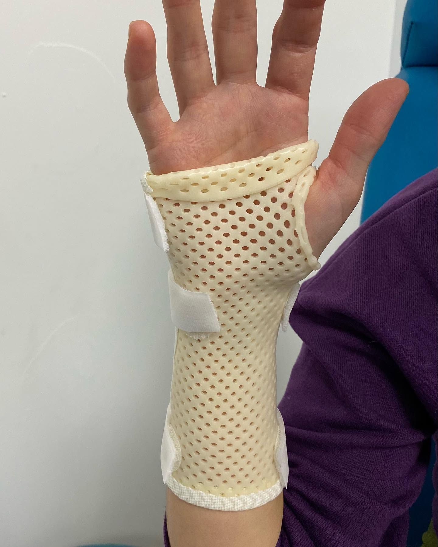 Main avec une attelle de poignet en maille blanche et un repose-pouce sur fond uni