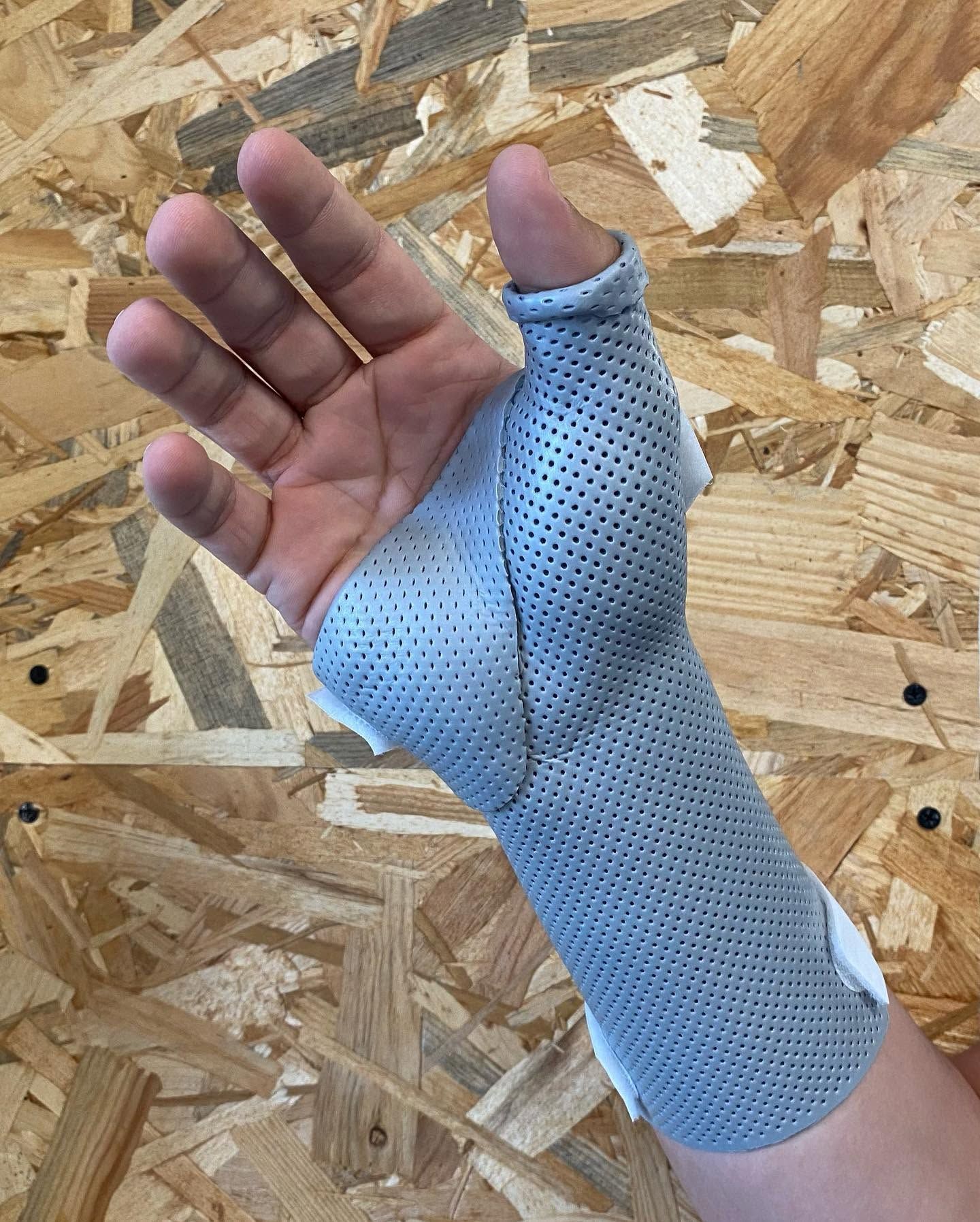 Main dans une attelle de poignet bleue perforée sur fond de panneau de bois OSB