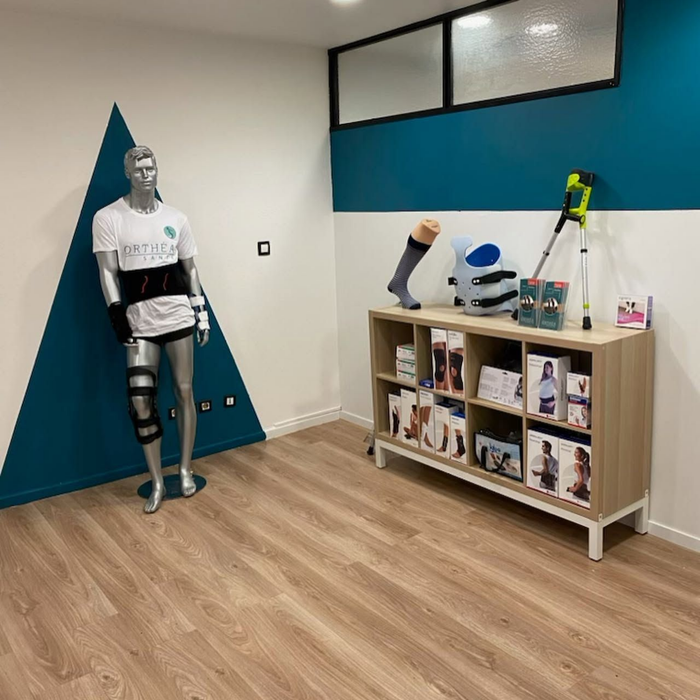 Mannequin blanc dans un cabinet médical, à côté d'une bibliothèque et de matériel médical posés sur un parquet.