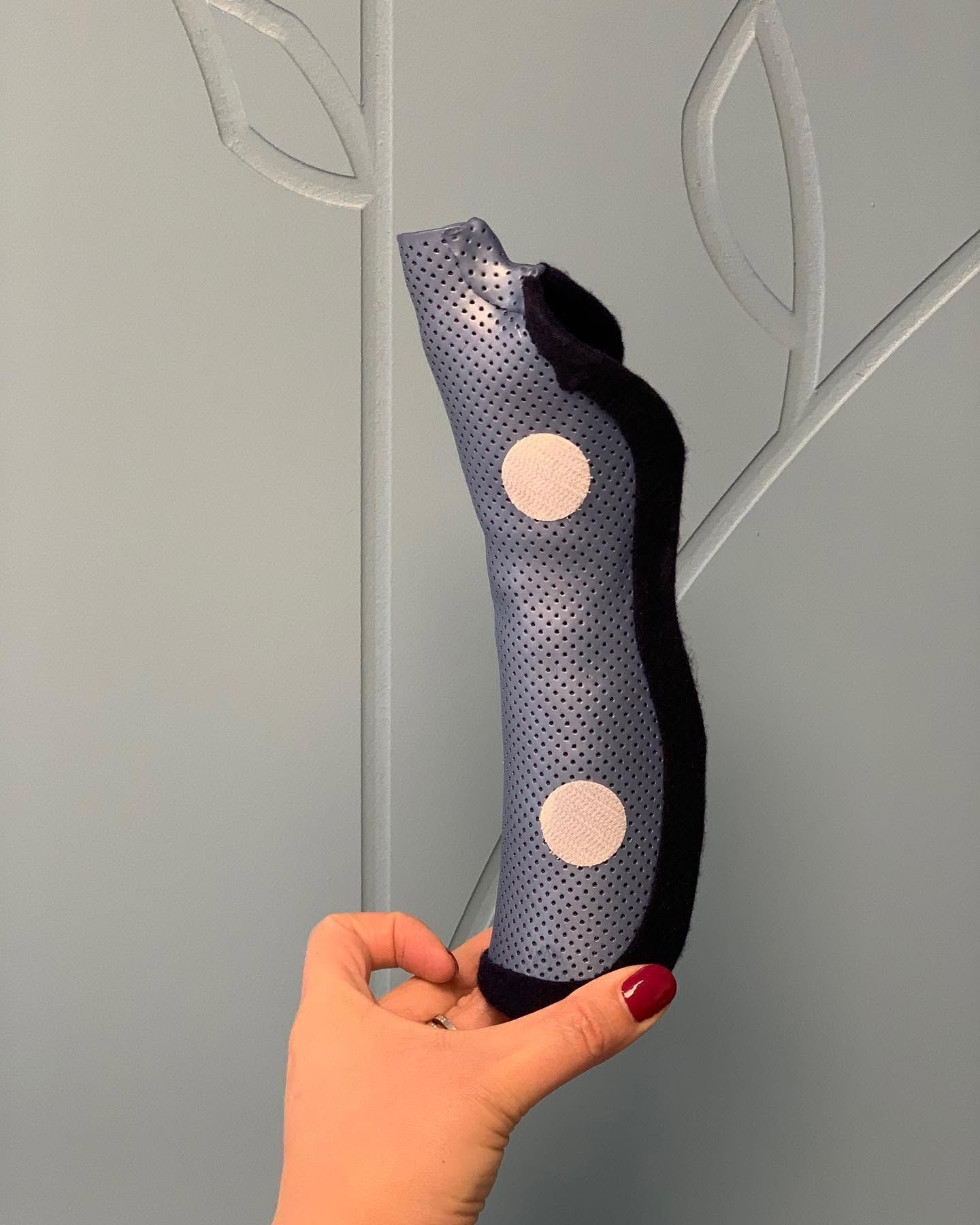 Main tenant une attelle orthopédique perforée bleu marine et noire avec deux coussinets blancs
