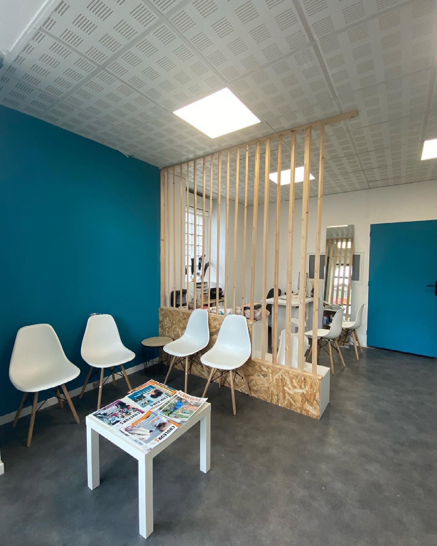 Hall d'entrée moderne avec chaises blanches, petite table, cloison en lattes de bois et murs d'accent bleus.