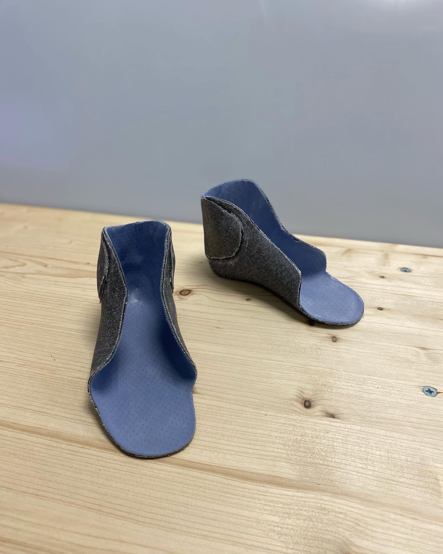 Une paire de petites orthèses moulées bleues et noires pour enfant sur une surface en bois.
