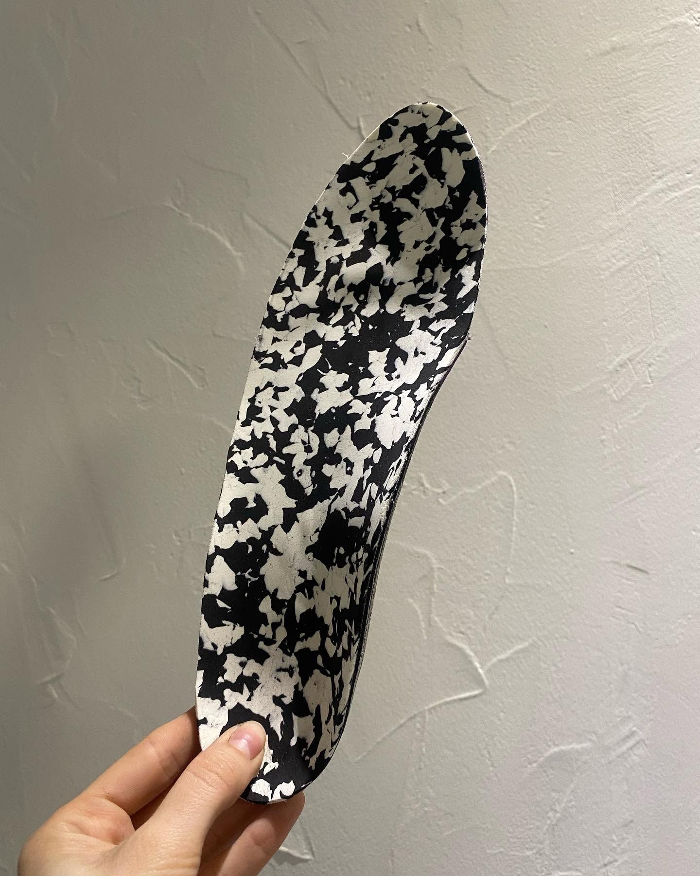 Main tenant une semelle intérieure à motifs noirs et blancs contre un mur texturé