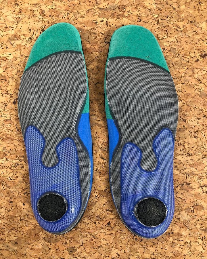 Paire de semelles bleues et grises avec embouts turquoise, présentées côte à côte sur une surface en liège.