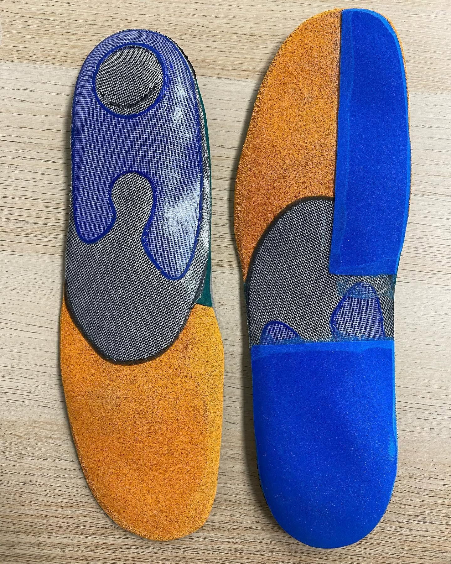 Deux semelles orthopédiques colorées, bleues, oranges et grises, présentées côte à côte sur un fond clair.