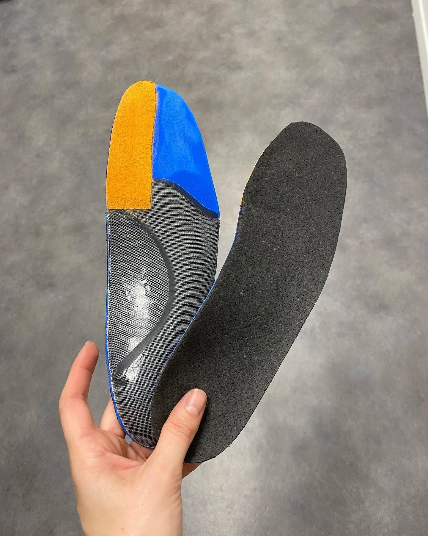 Main tenant une paire de semelles noires avec renforts bleus et oranges.