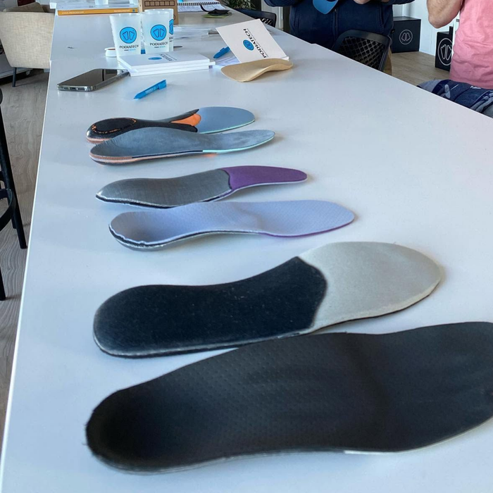 Semelles et inserts de chaussures disposés sur une table dans un atelier ou une salle d'exposition.