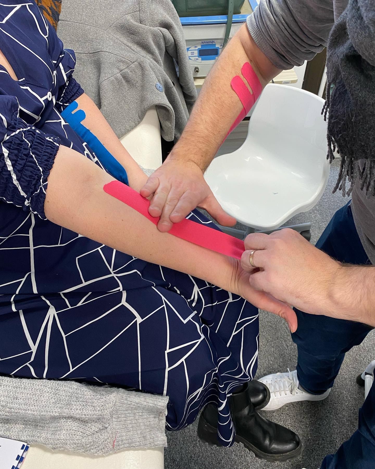 Deux personnes appliquent des bandes de strapping rose sur un bras