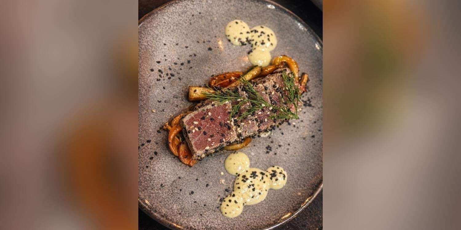 Filete sellado en un plato moteado con guarnición de hierbas y puntos de salsa cremosa.