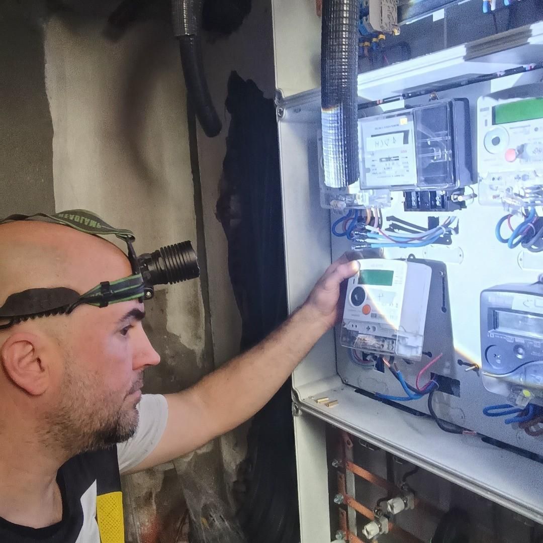 Técnico inspeccionando un panel de control eléctrico con linterna frontal en un cuarto de servicio.