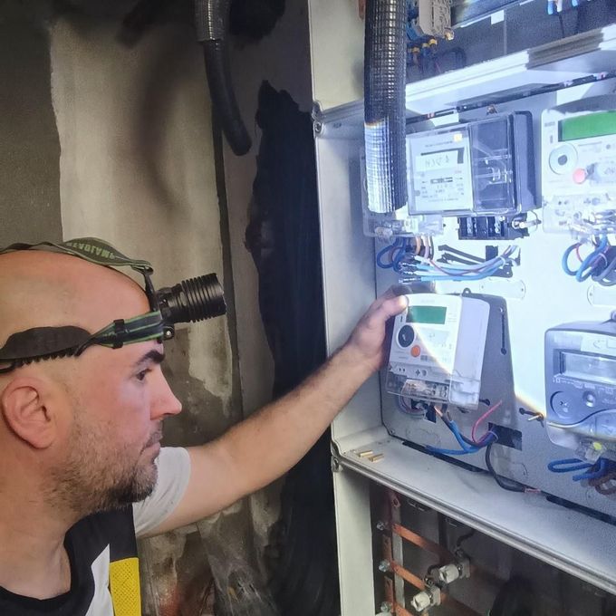 Técnico inspeccionando un panel de control eléctrico con linterna frontal en un cuarto de servicio.