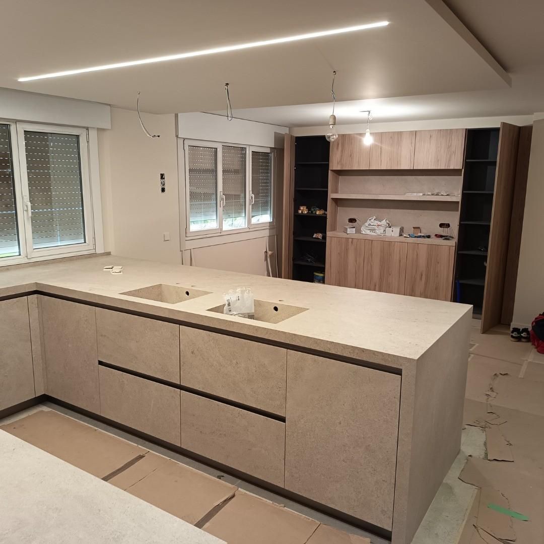 Cocina moderna con isla grande, encimeras blancas, armarios de madera y estanterías empotradas en proceso de renovación.
