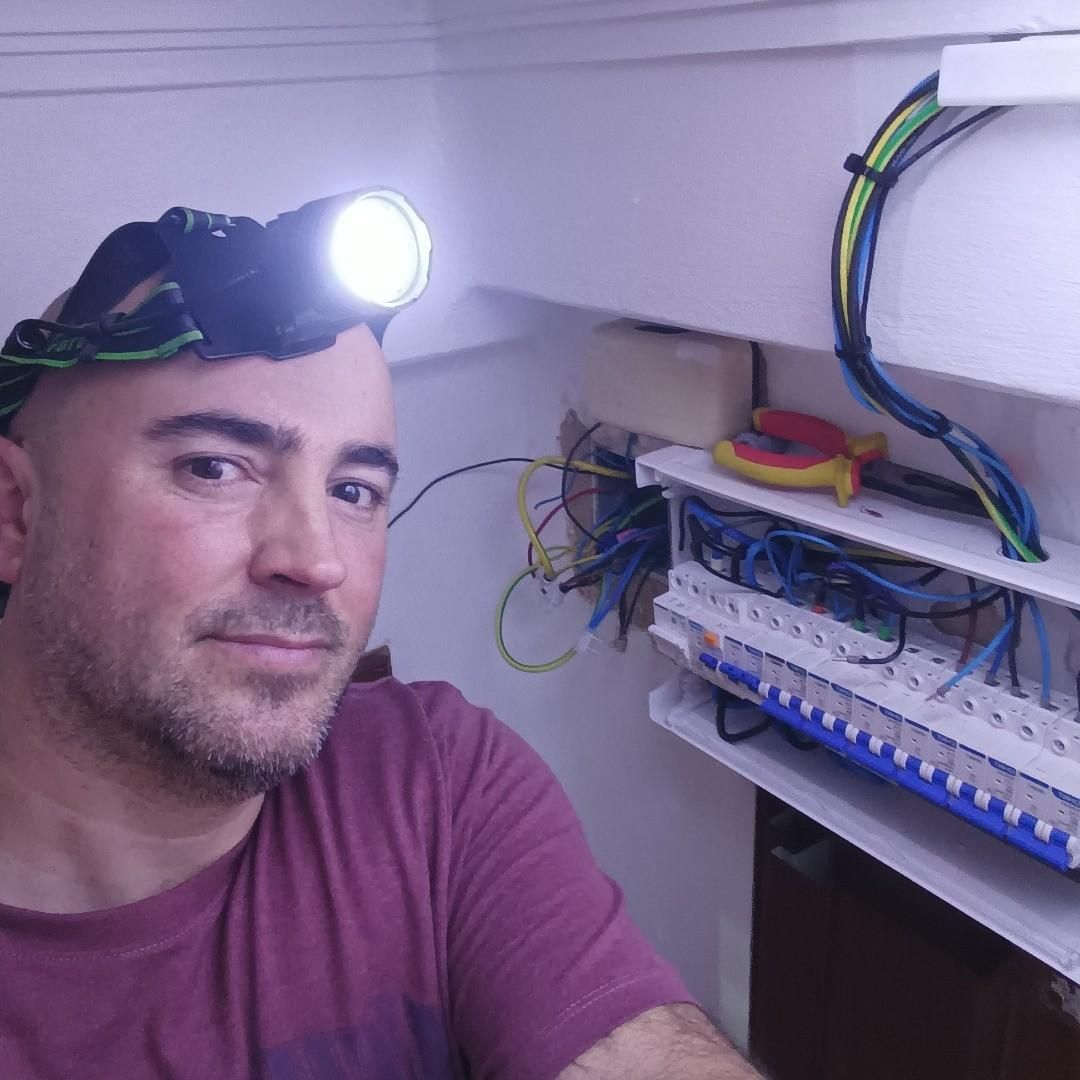 Hombre con linterna frontal en una habitación junto a un panel eléctrico abierto con cableado expuesto.