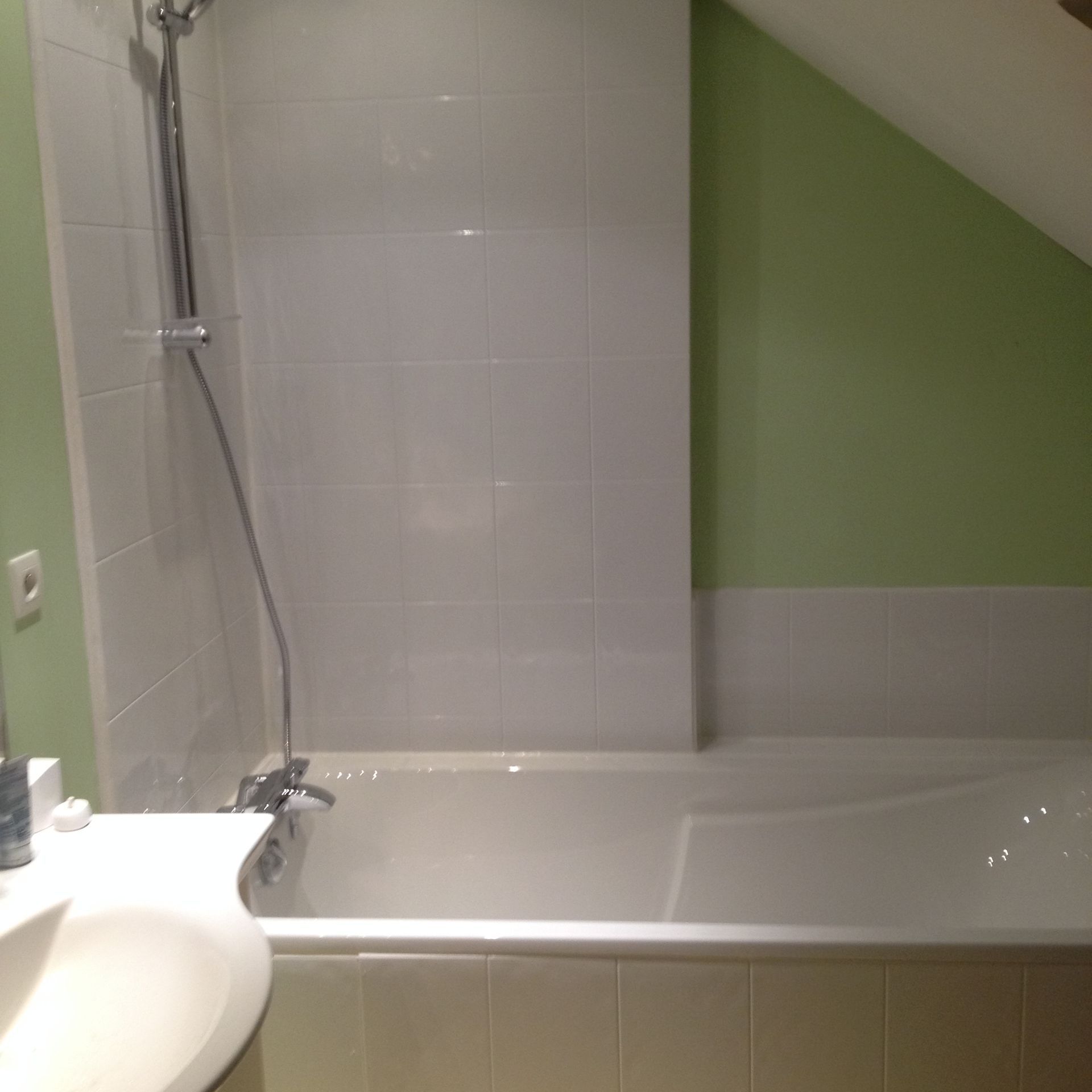 Baignoire avec pommeau de douche et partie carrelée sur le mur dans l'angle