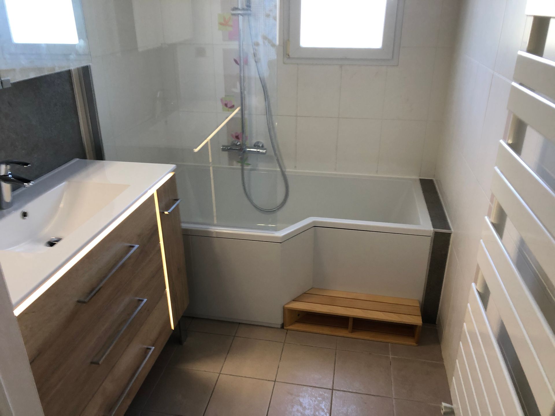 Même salle de bains avec une baignoire munie d'une marche et d'une paroi vitrée, sèche-serviettes sur le côté