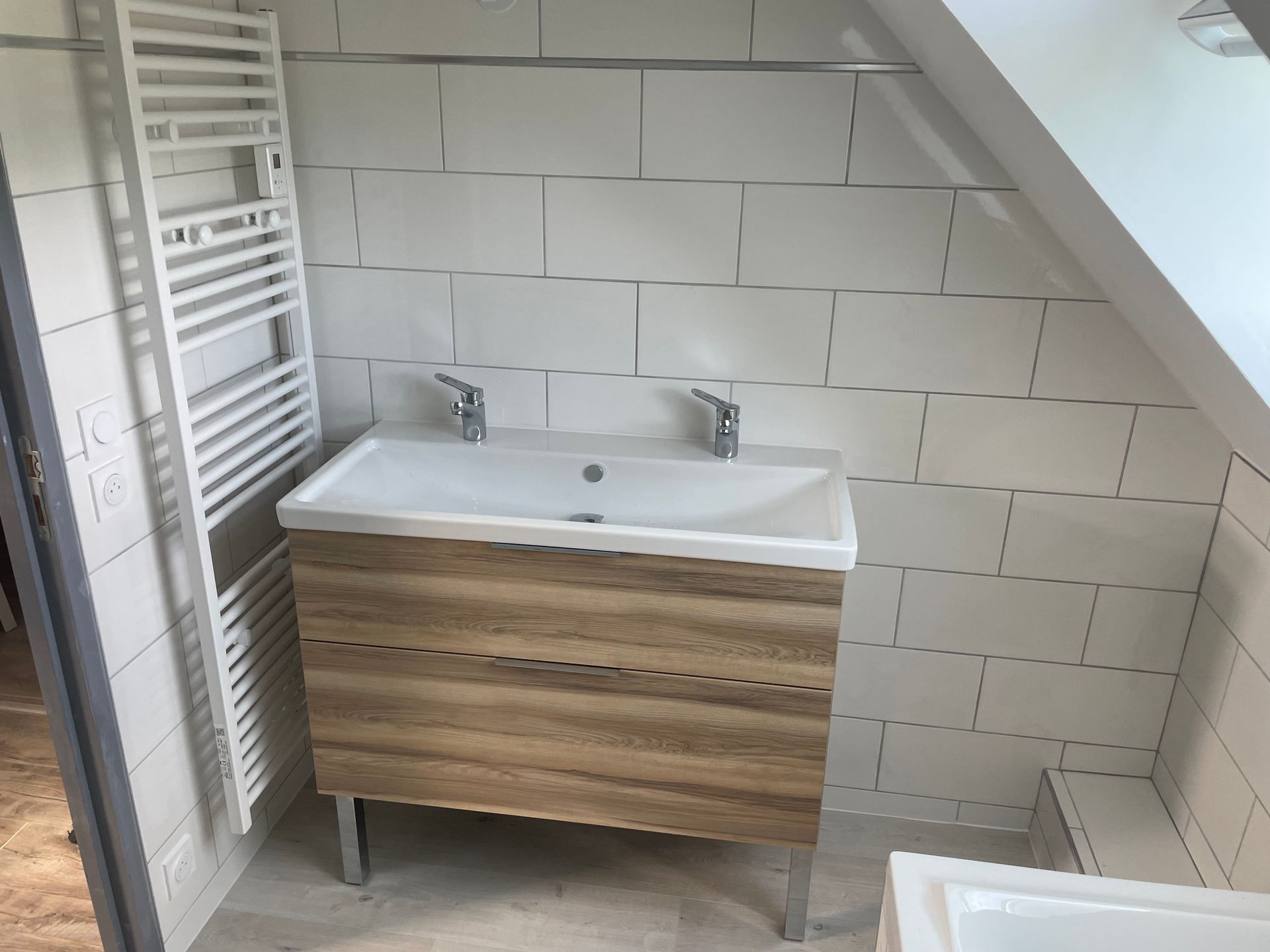 Salle de bains avec murs carrelés, meuble avec doubles vasques et sèche-serviettes sur le côté