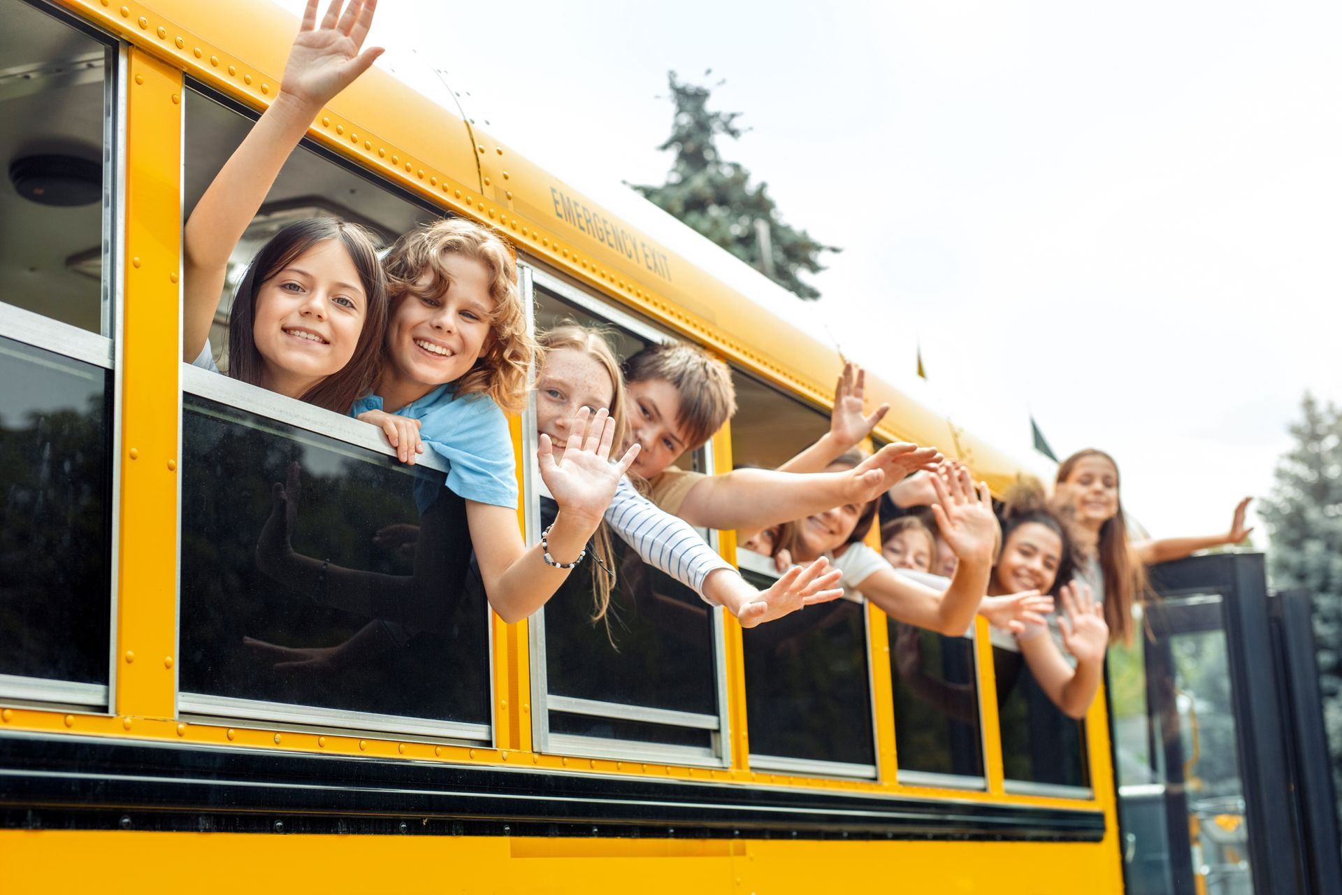 Eine Gruppe Kinder winkt aus den Fenstern eines Schulbusses.