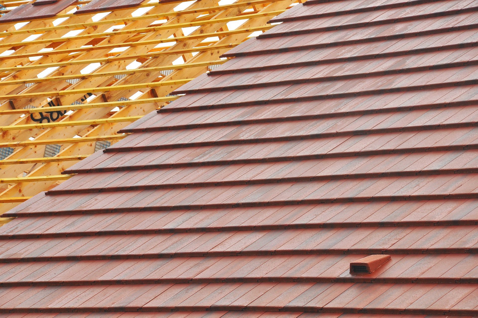 Toiture partiellement recouverte de tuiles rouges, laissant apparaître la charpente en bois sous-jacente lors de la pose.