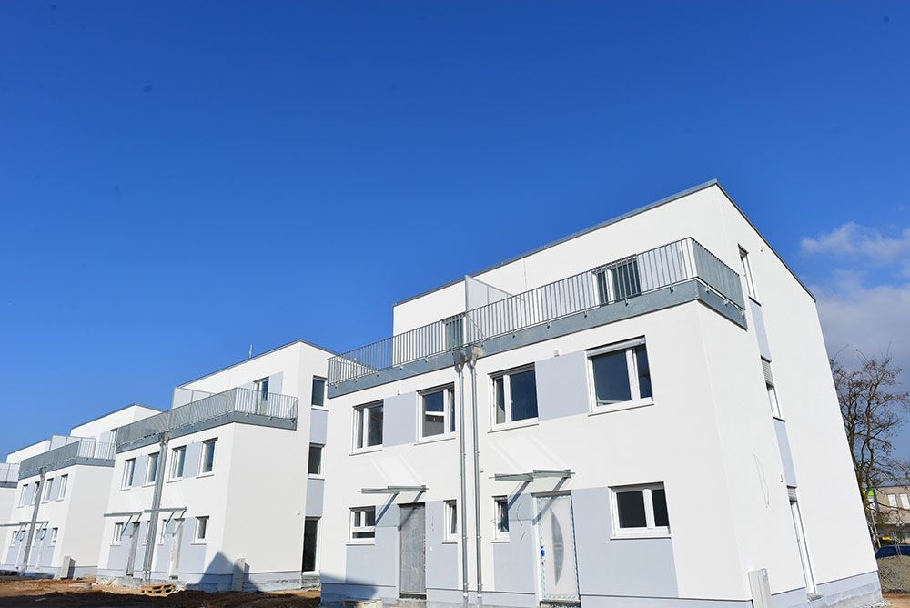 Moderne, weiße Stadthäuser mit Balkonen unter strahlend blauem Himmel.