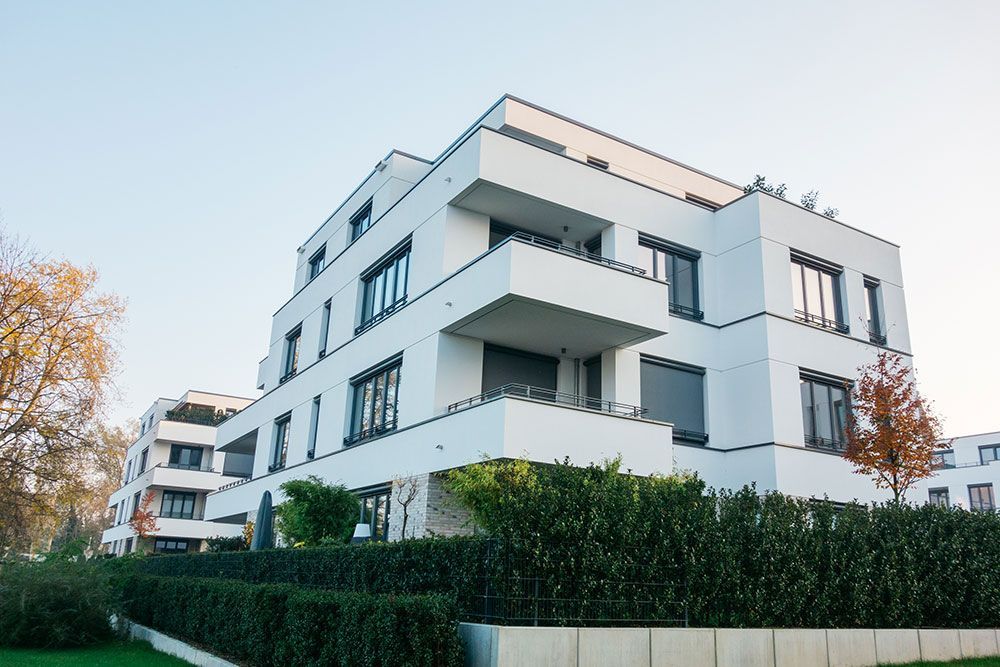 Modernes, weißes, mehrstöckiges Wohnhaus mit Balkonen, blauer Himmel im Hintergrund.