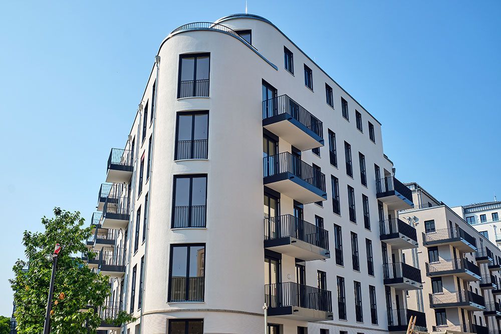 Weißes, modernes Apartmentgebäude mit Balkonen unter blauem Himmel.