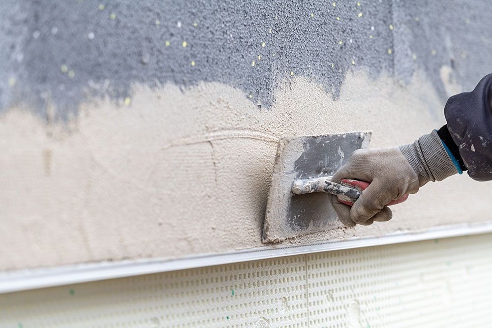 Eine Person mit Handschuhen trägt mit einer Kelle Stuck auf eine Wand auf.