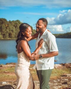 Un couple s'embrasse au bord d'un lac par une journée ensoleillée ; la femme en robe crème.