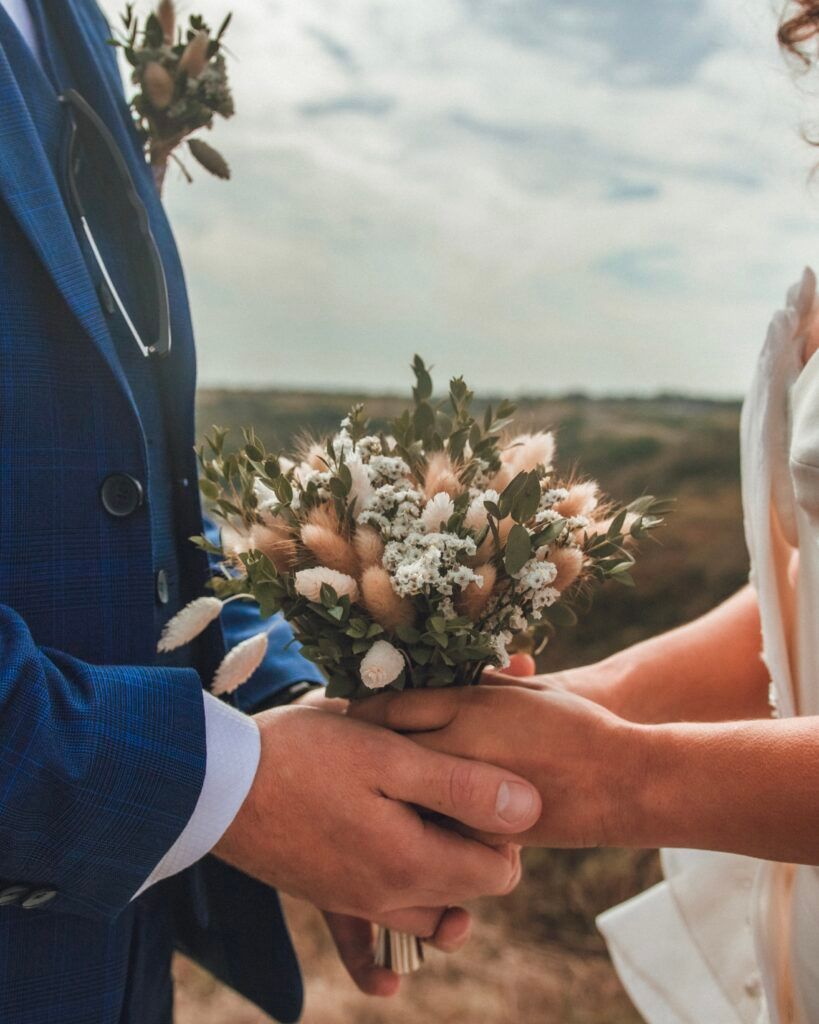 Couple se tenant la main, petit bouquet de fleurs, extérieur, journée ensoleillée.