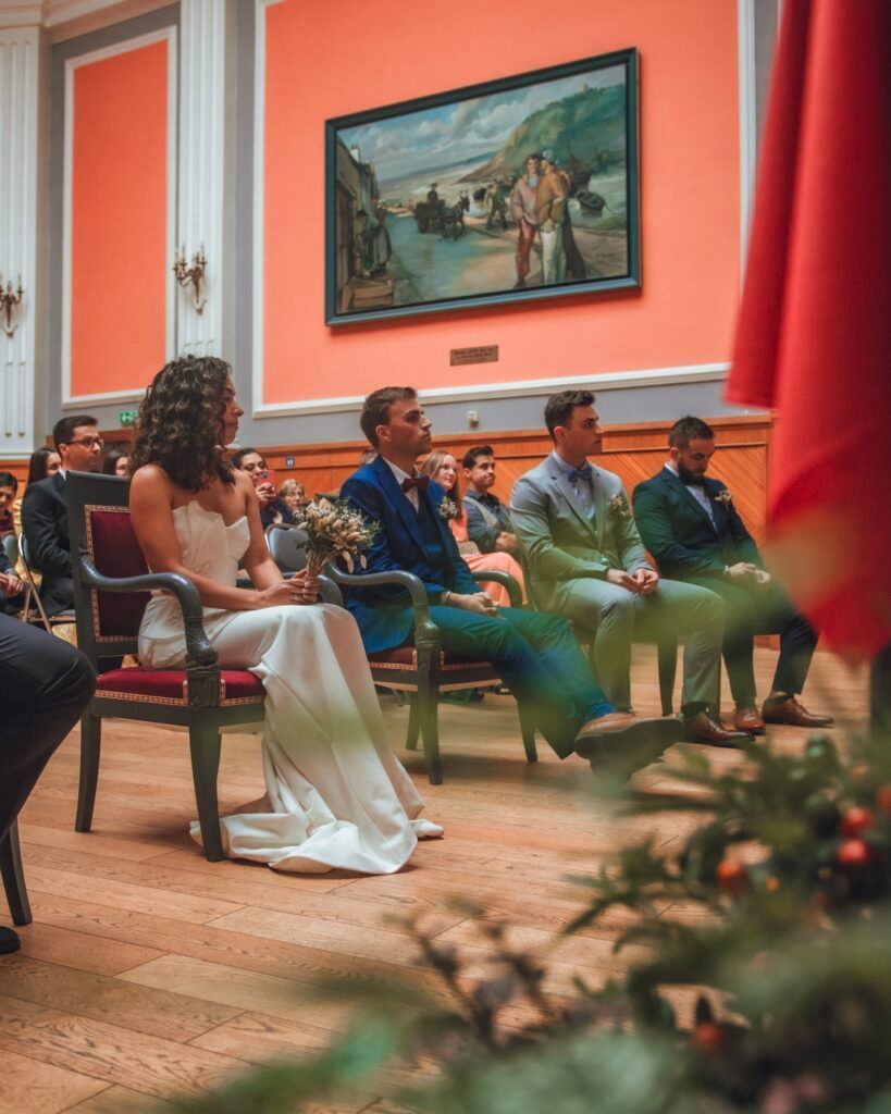 Une mariée en robe blanche est assise lors d'une cérémonie de mariage ; les garçons d'honneur sont assis en arrière-plan.
