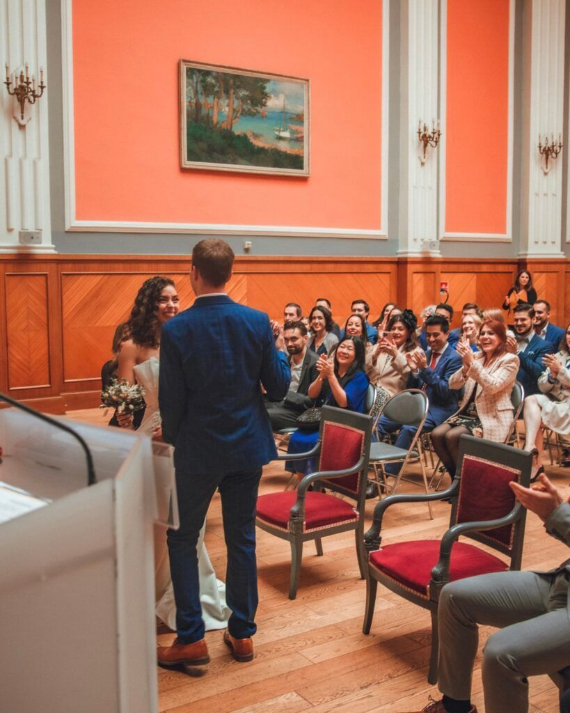 Couple lors d'une cérémonie de mariage, face à face, les invités applaudissent dans une salle formelle.
