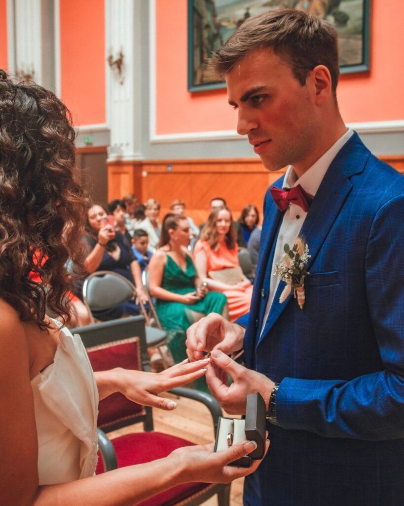 Le marié en costume bleu passe l'alliance au doigt de la mariée lors d'une cérémonie de mariage.