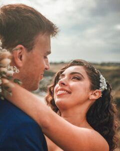 Un couple s'embrasse dehors, se regardant avec amour. La femme sourit, coiffée d'un chapeau ; l'homme l'entoure de son bras.