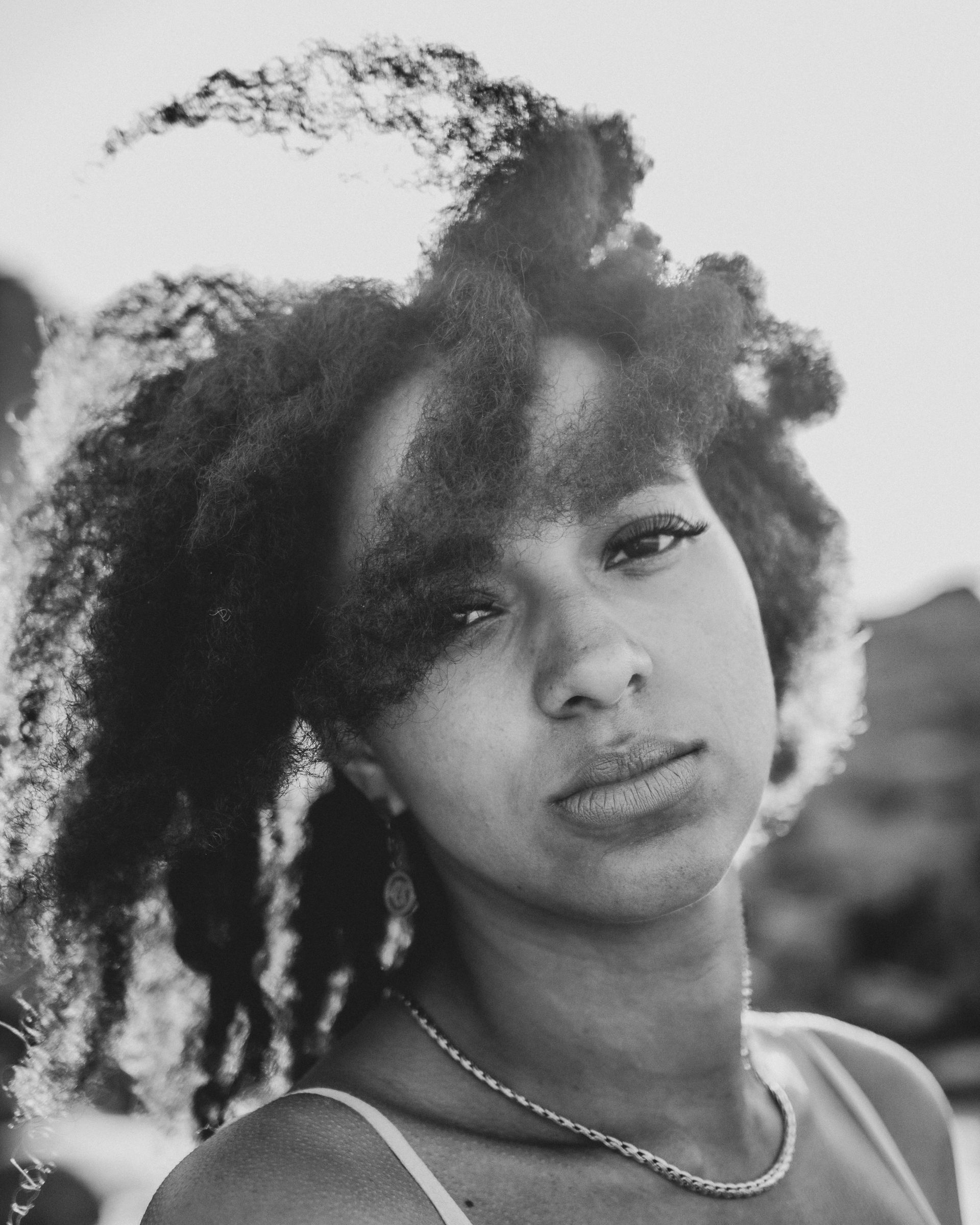 Portrait en noir et blanc d'une femme aux cheveux bouclés regardant l'objectif. Elle porte un collier et un débardeur.