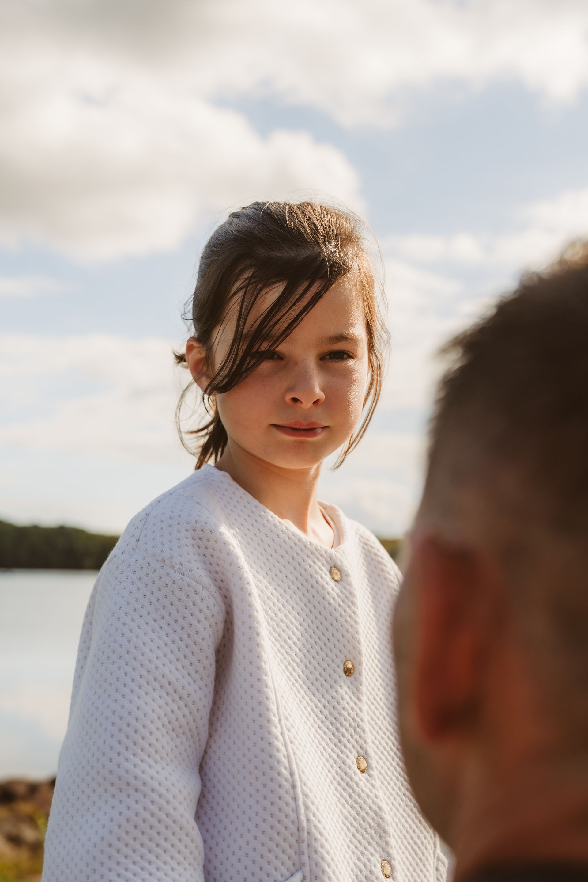Jeune fille en pull blanc regardant l'objectif, lac et ciel en arrière-plan.