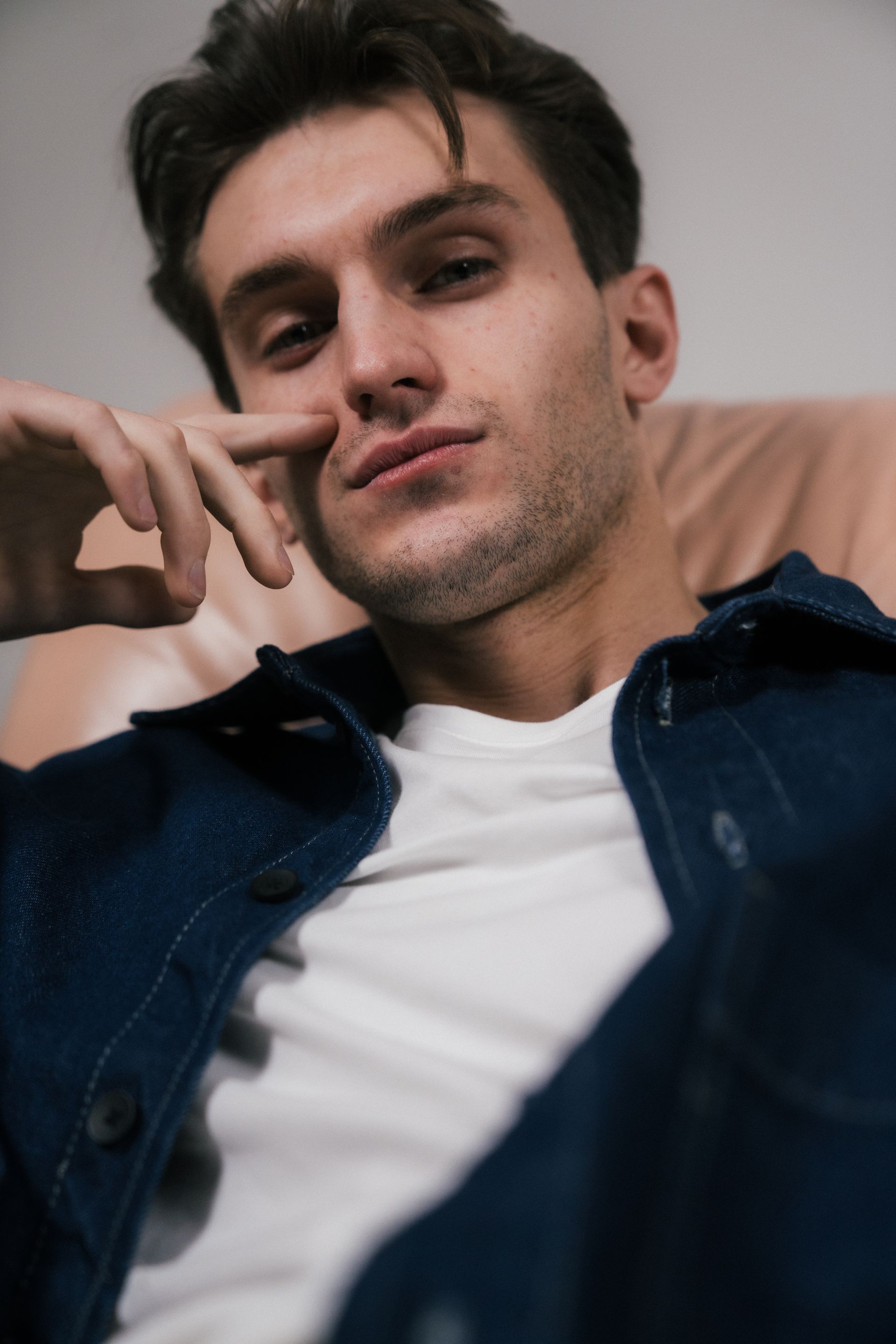 Un homme en veste en jean, le menton posé sur la main, regarde le spectateur avec une expression pensive.