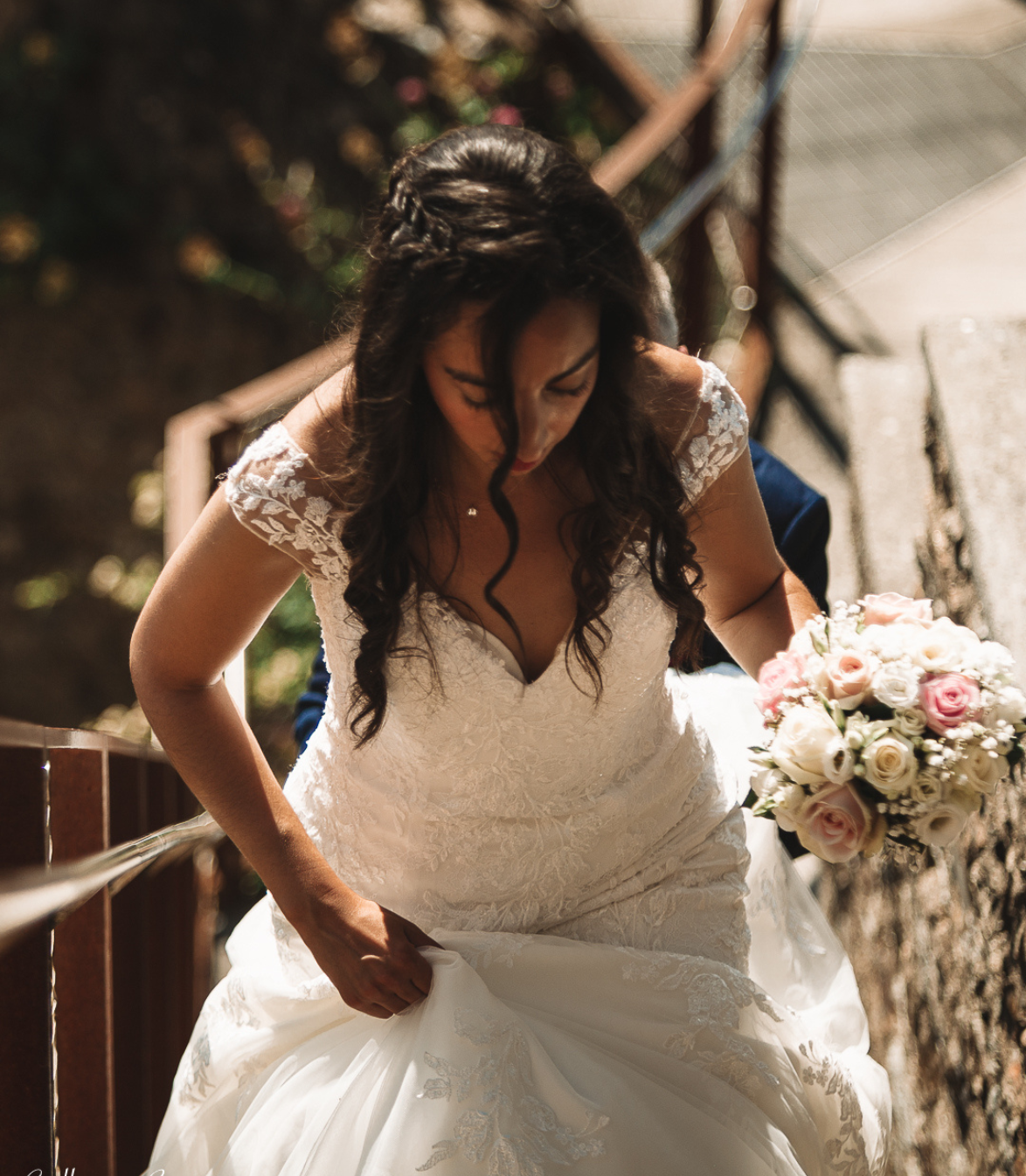 La mariée en robe de mariée blanche descend des marches en pierre, tenant sa jupe et son bouquet de fleurs roses et blanches.