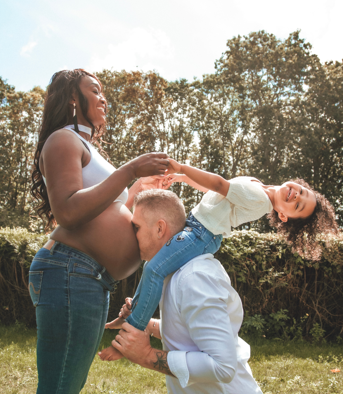 Une femme enceinte et un homme avec un enfant jouent dans la cour. La femme touche son ventre.
