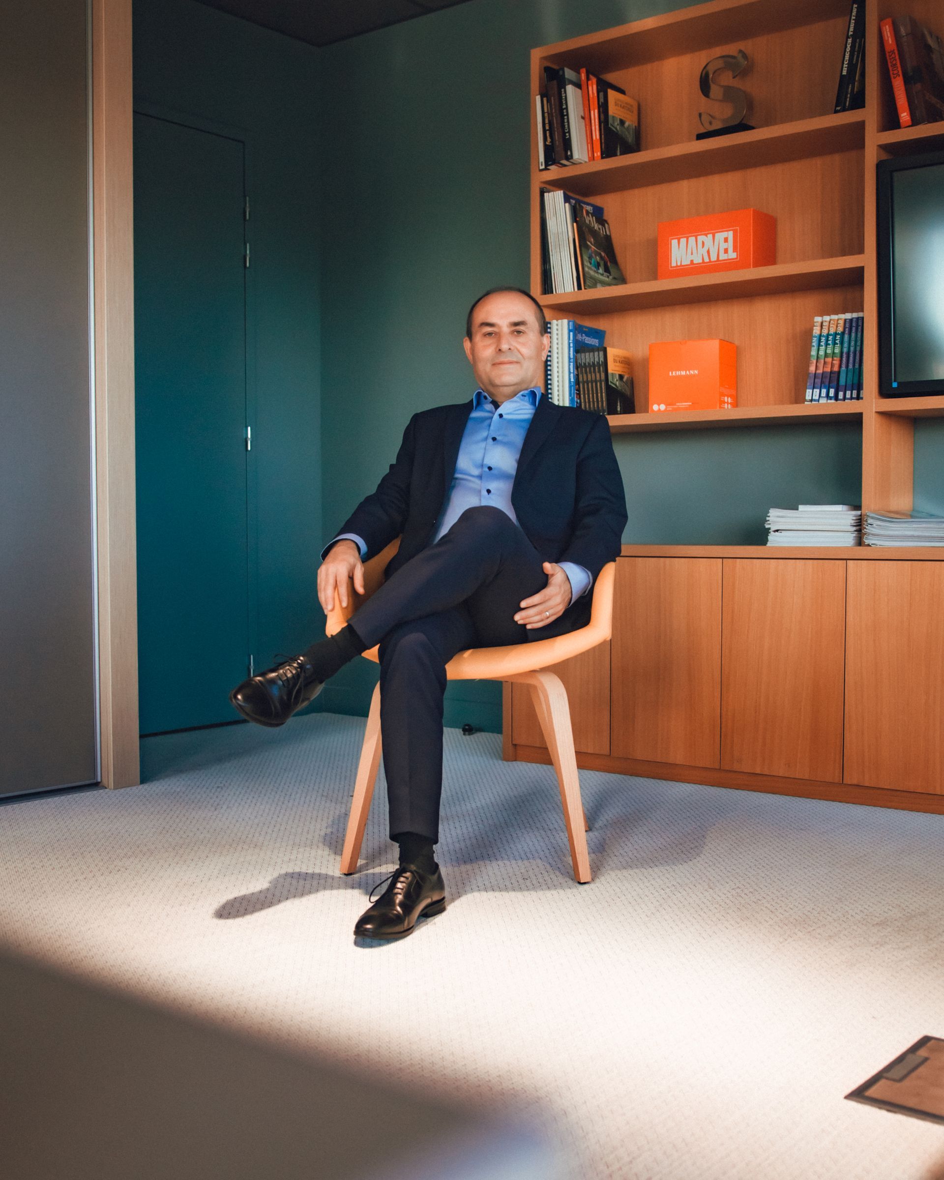 Un homme en costume est assis les jambes croisées sur une chaise dans un bureau moderne.