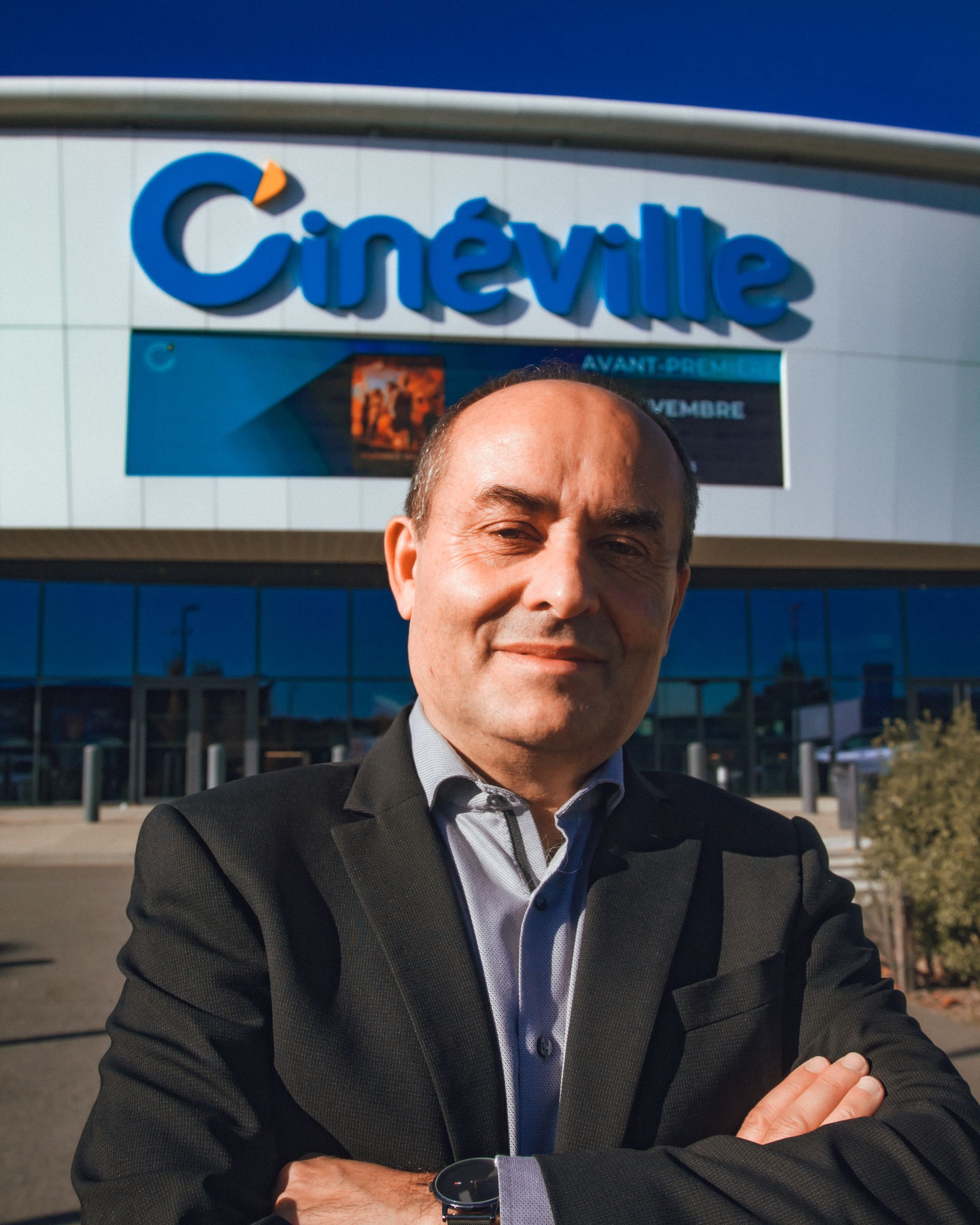 Un homme en costume se tient devant le cinéma Cinêville, panneau bleu visible.