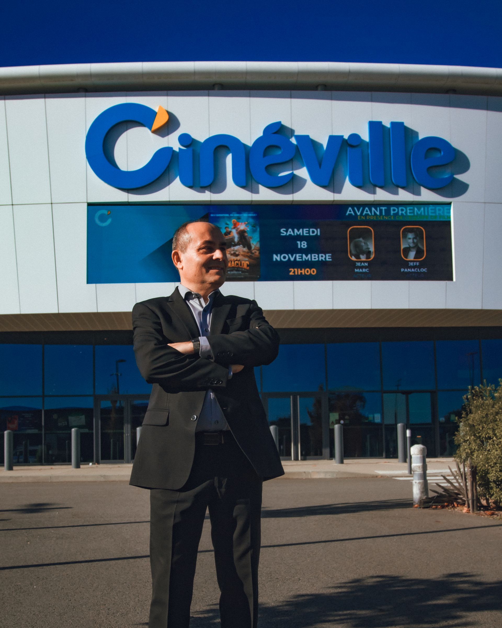 Un homme en costume se tient devant le cinéma Cinéville, les bras croisés.