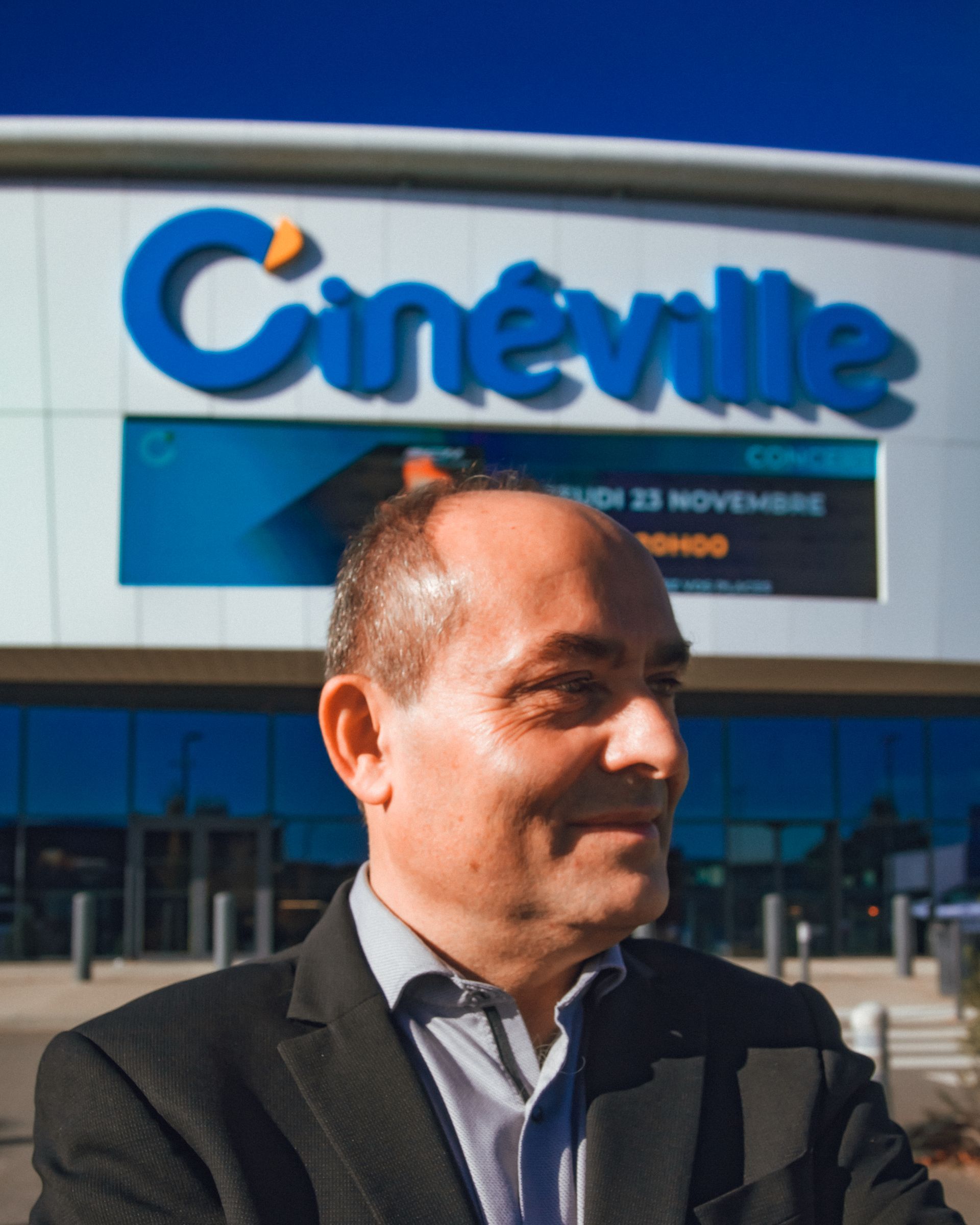 Un homme en costume sourit devant le bâtiment du cinéma
