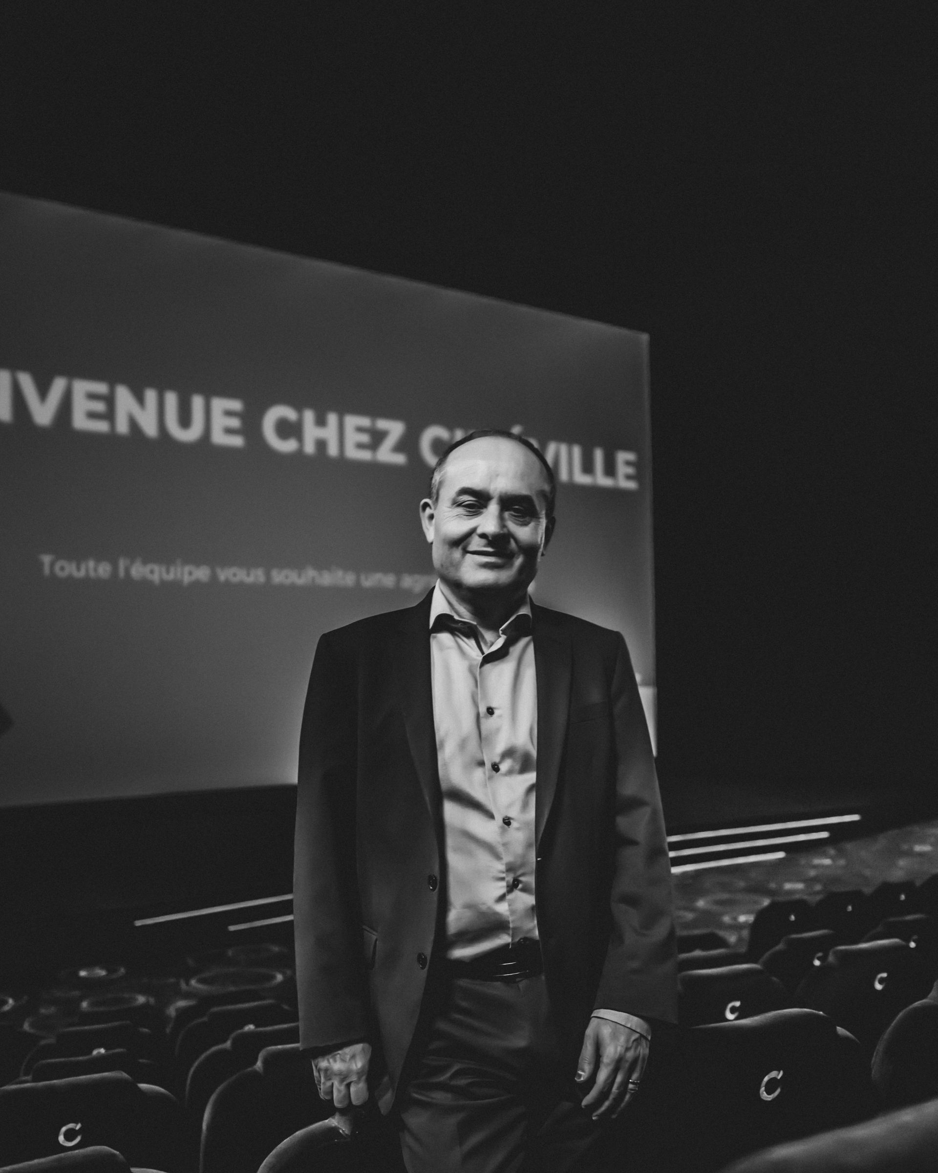 Un homme en costume se tient dans un cinéma avec un écran sur lequel on peut lire « Bienvenue chez Cineville ».