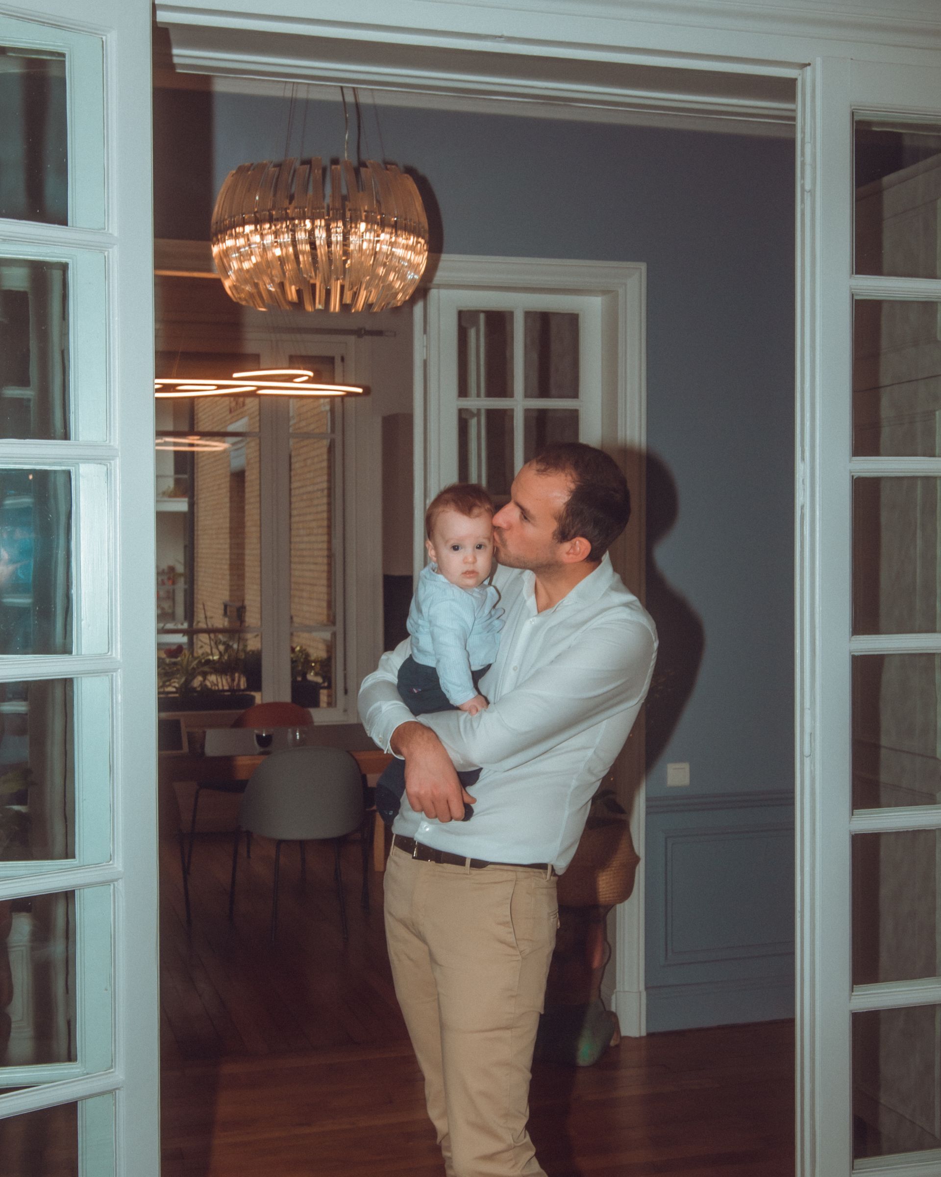 Homme embrassant un bébé, debout dans l'embrasure de la porte ; intérieur de maison moderne.