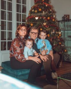 Famille de quatre personnes assise devant le sapin de Noël. Un homme et une femme tiennent deux jeunes.