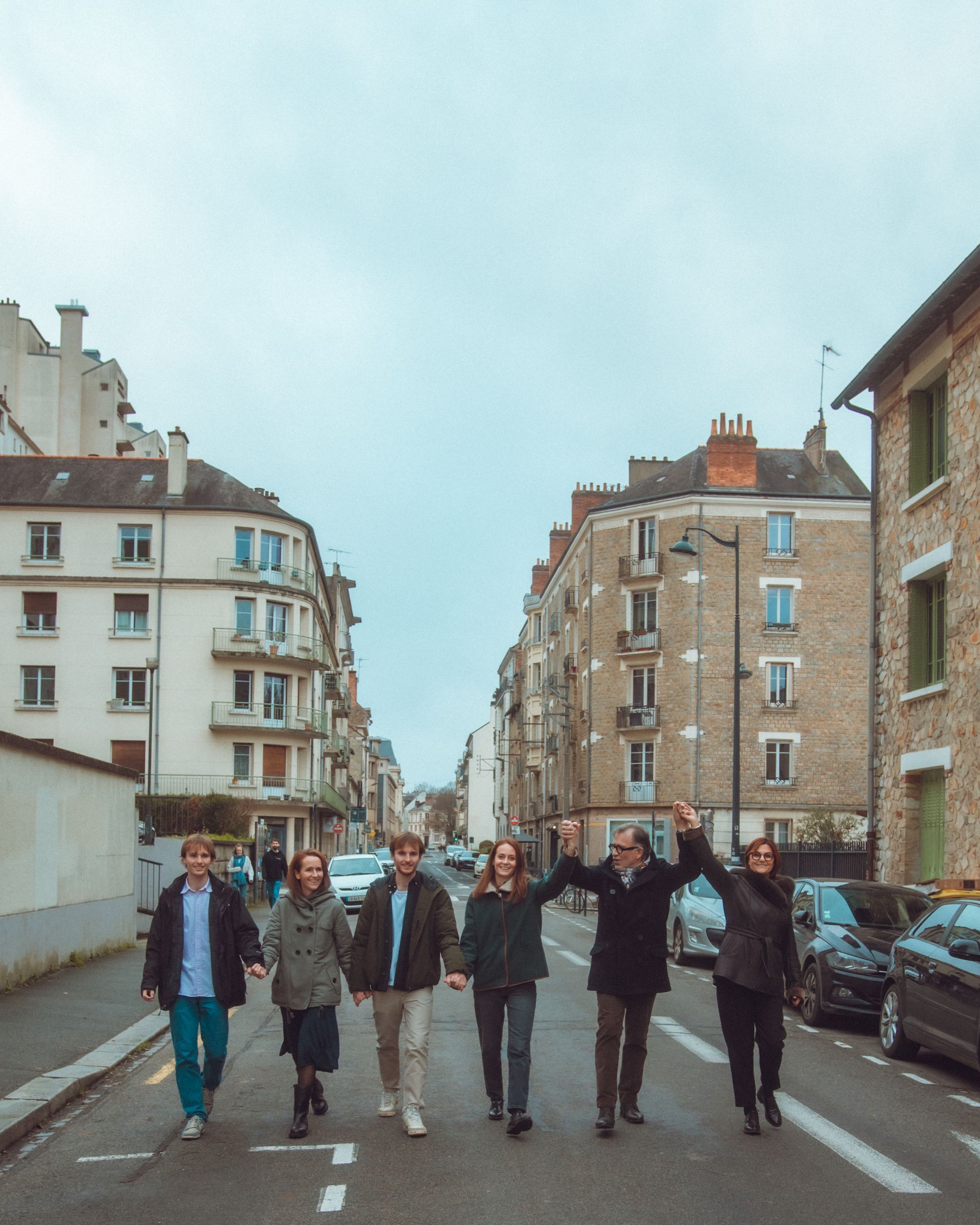 Six personnes marchent dans la rue d'une ville européenne, main dans la main, bras levés. Journée nuageuse.