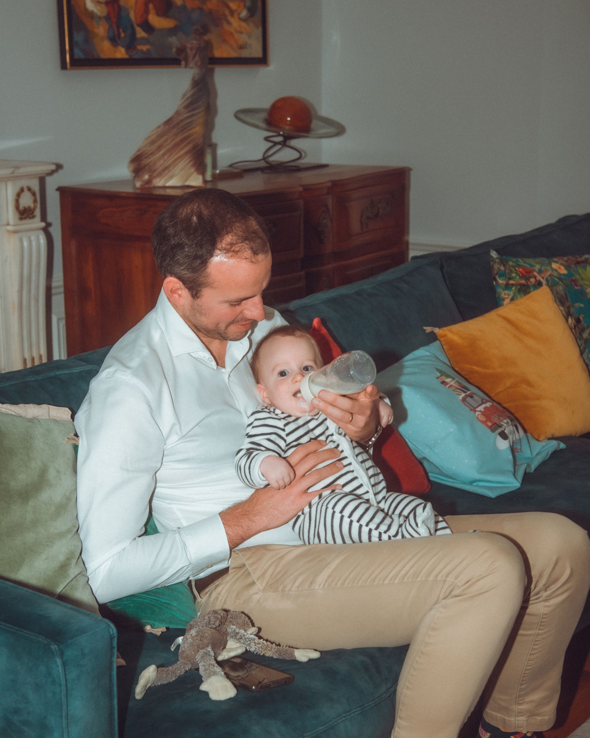 Un homme donne le biberon à un bébé sur un canapé bleu.