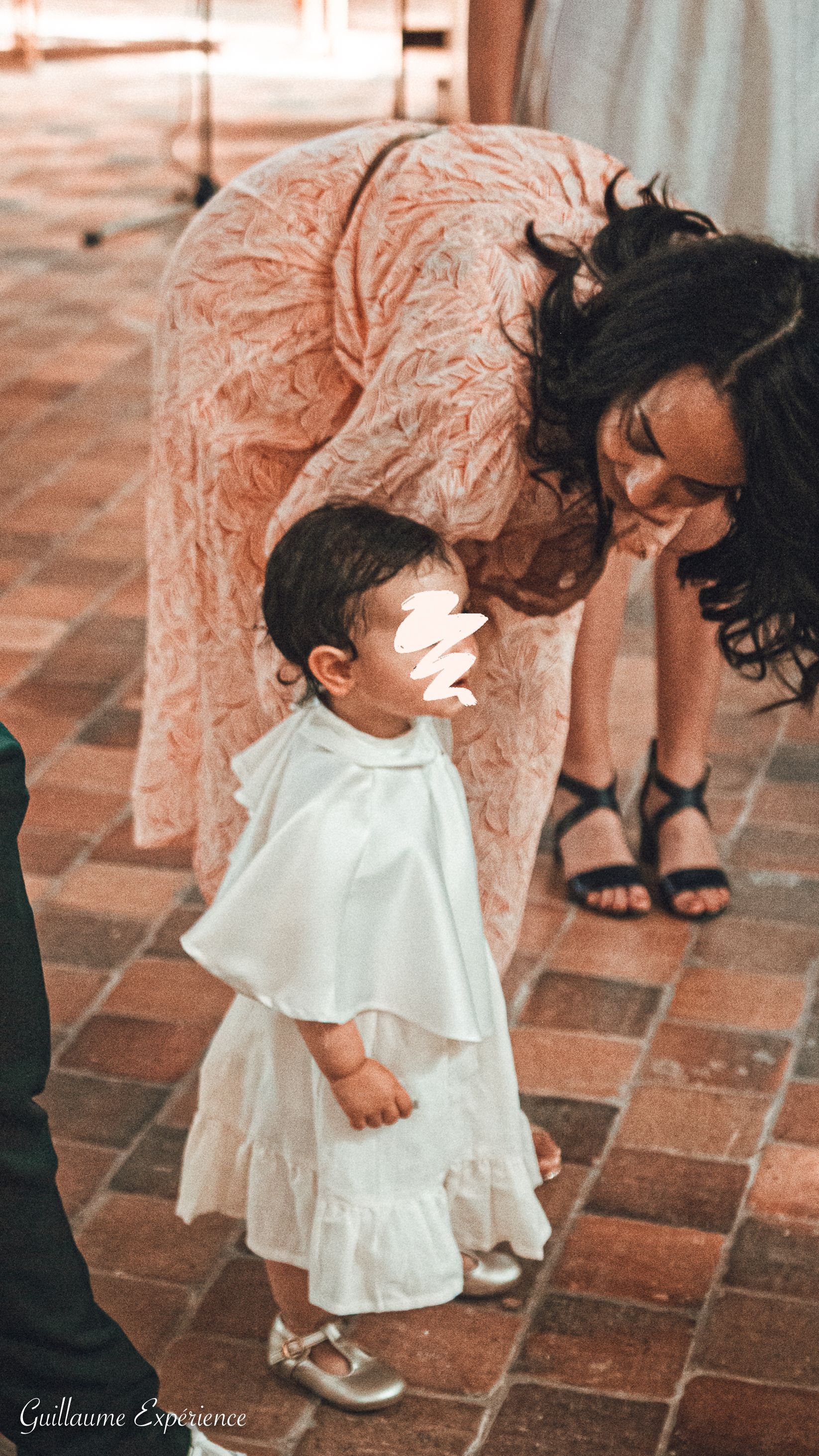 Femme et enfant en tenues blanches assorties à l'intérieur ; la femme se penche vers l'enfant.