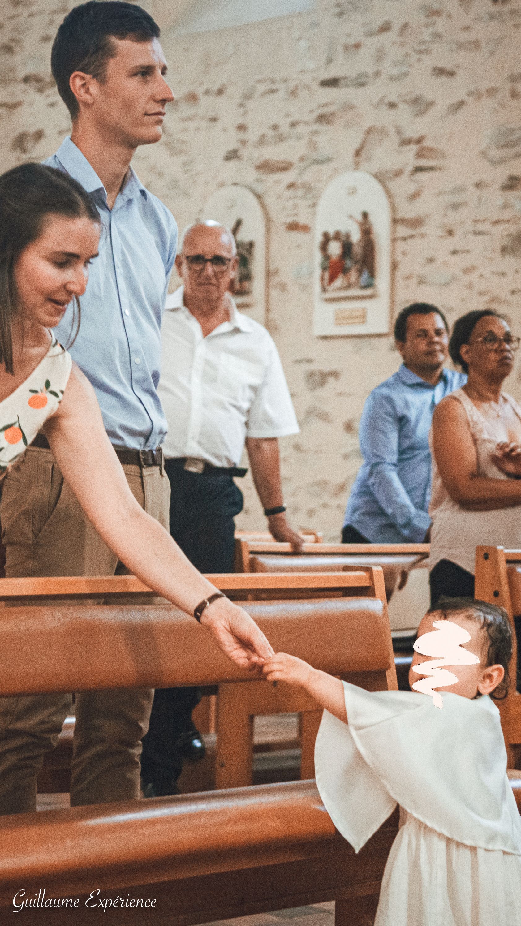 Une femme tend la main à un enfant lors d'une cérémonie religieuse. Des personnes sont présentes à l'arrière-plan.